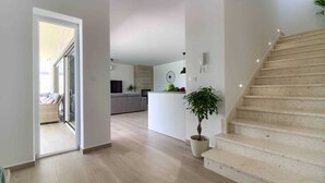 Un interior moderno con una escalera, una zona de cocina y un espacio de estar con un sofá y una mesa de comedor.