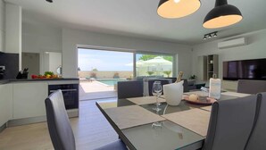 Una cocina moderna con comedor, un ventanal grande y vistas a una piscina y follaje.