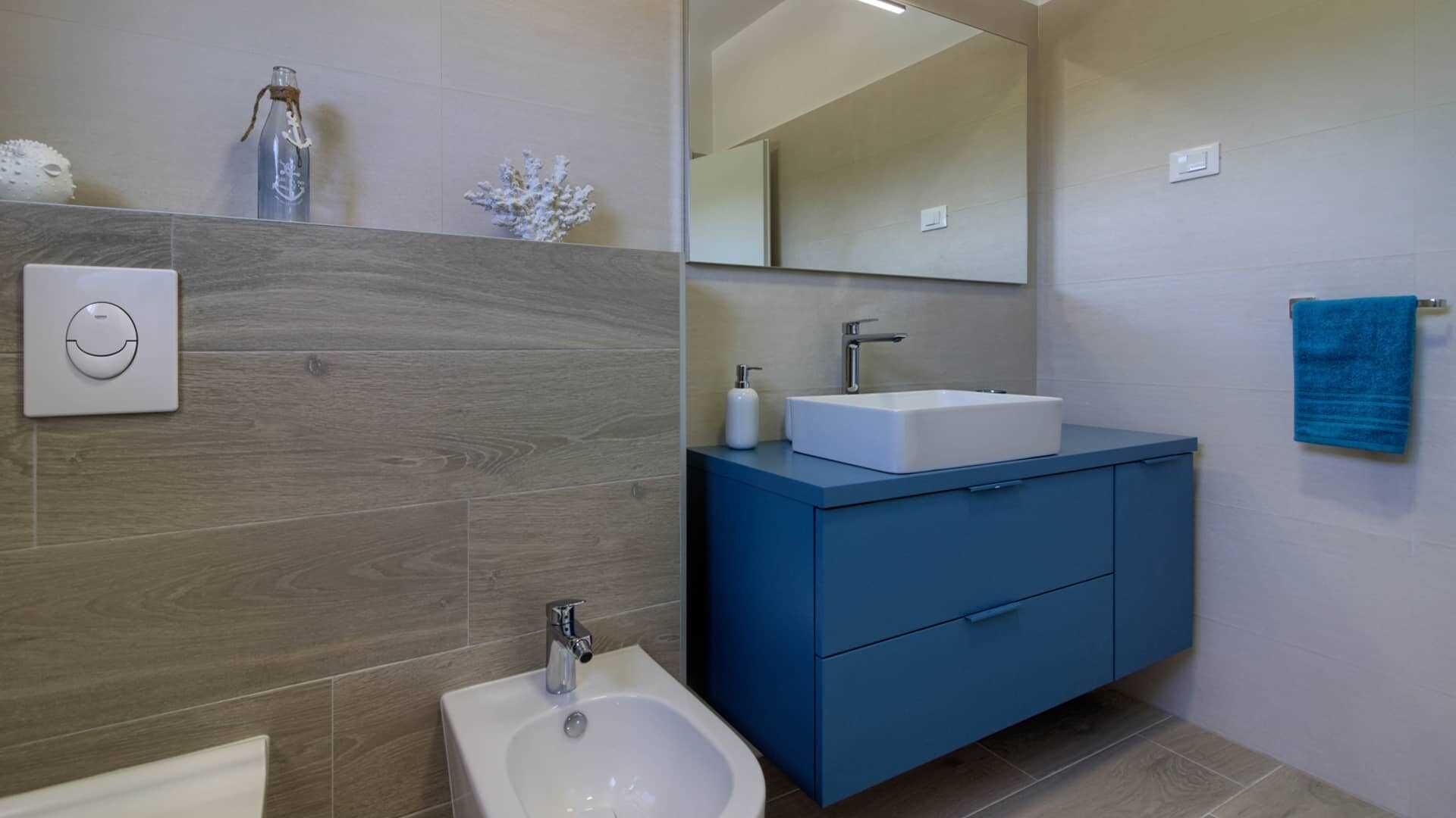 Une salle de bain moderne avec un bidet, un lavabo blanc, un meuble-lavabo bleu et un grand miroir.