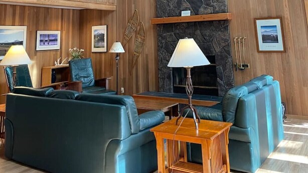 A spacious lobby with high ceilings, wooden paneling, a stone fireplace, and a seating area with blue sofas and a wooden coffee table. - Woodzy Retreat Getaway (Black Butte Ranch)