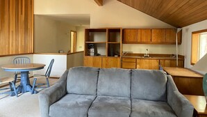 A cozy living room with a grey sofa, wooden cabinets, and a dining table with chairs. - Woodzy Retreat Getaway (Black Butte Ranch)