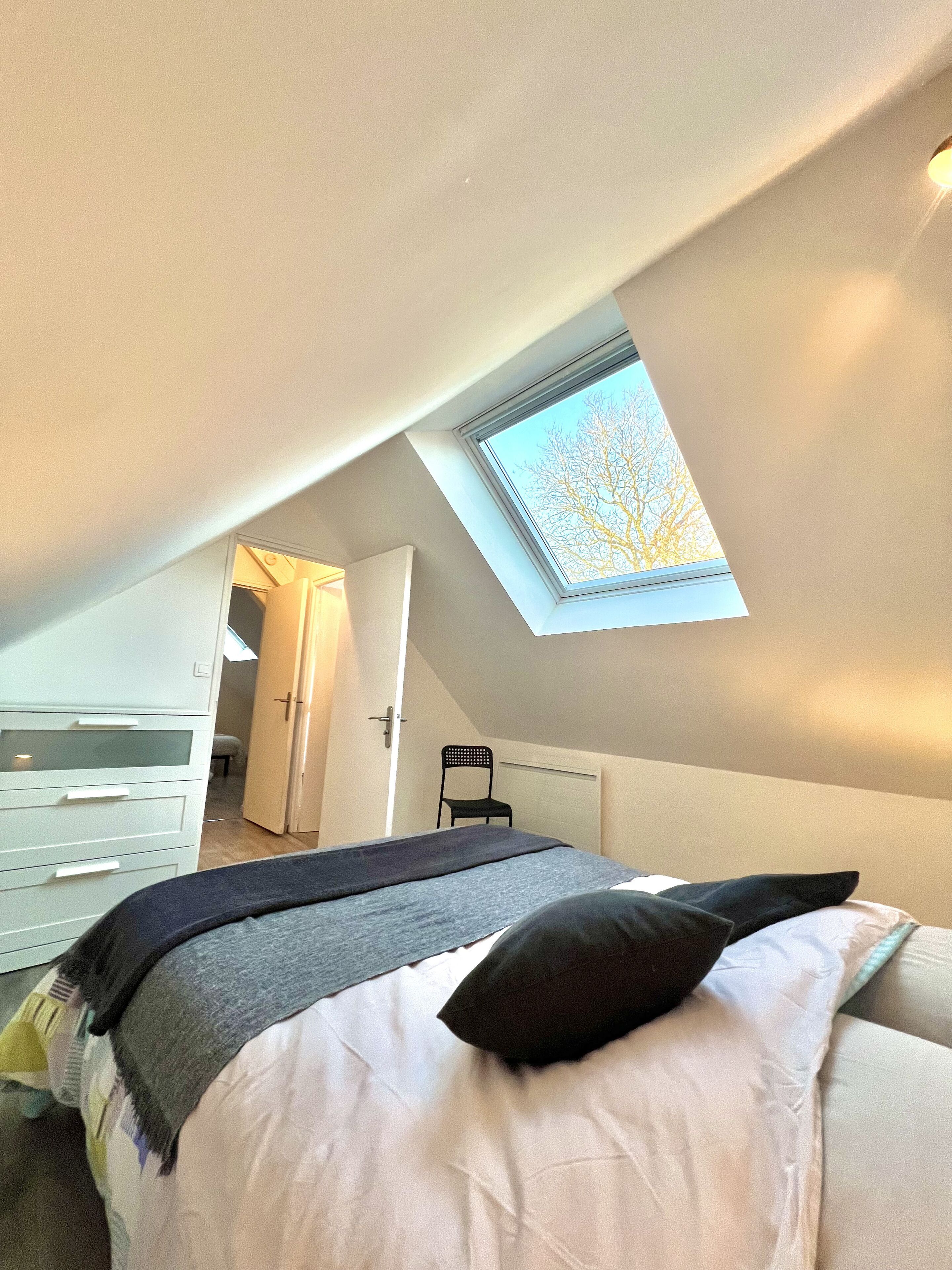 A bedroom with a skylight, a bed with pillows, a chair, and a dresser.