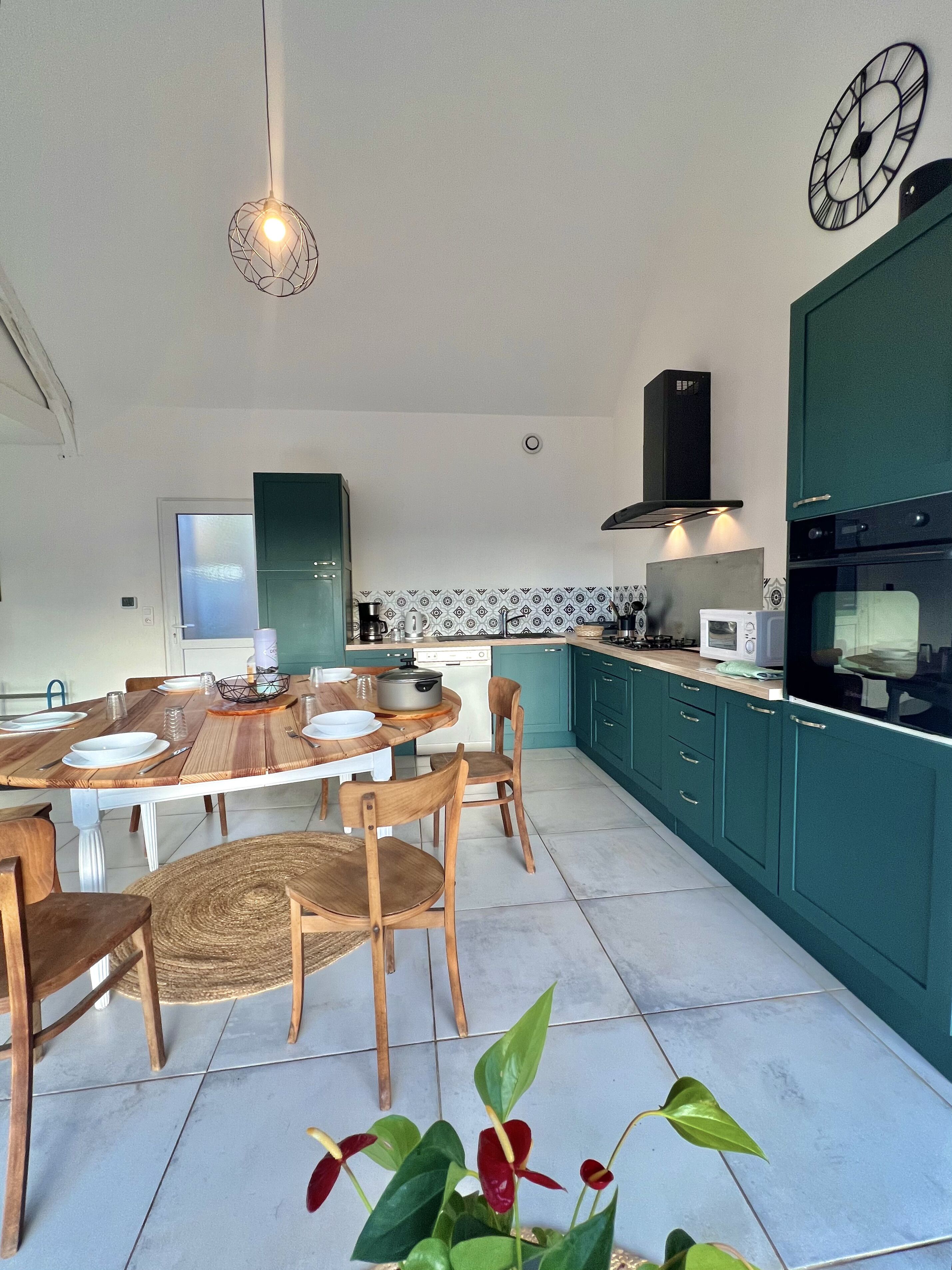 Une cuisine moderne avec des meubles de couleur turquoise, une table à manger en bois et un luminaire suspendu.