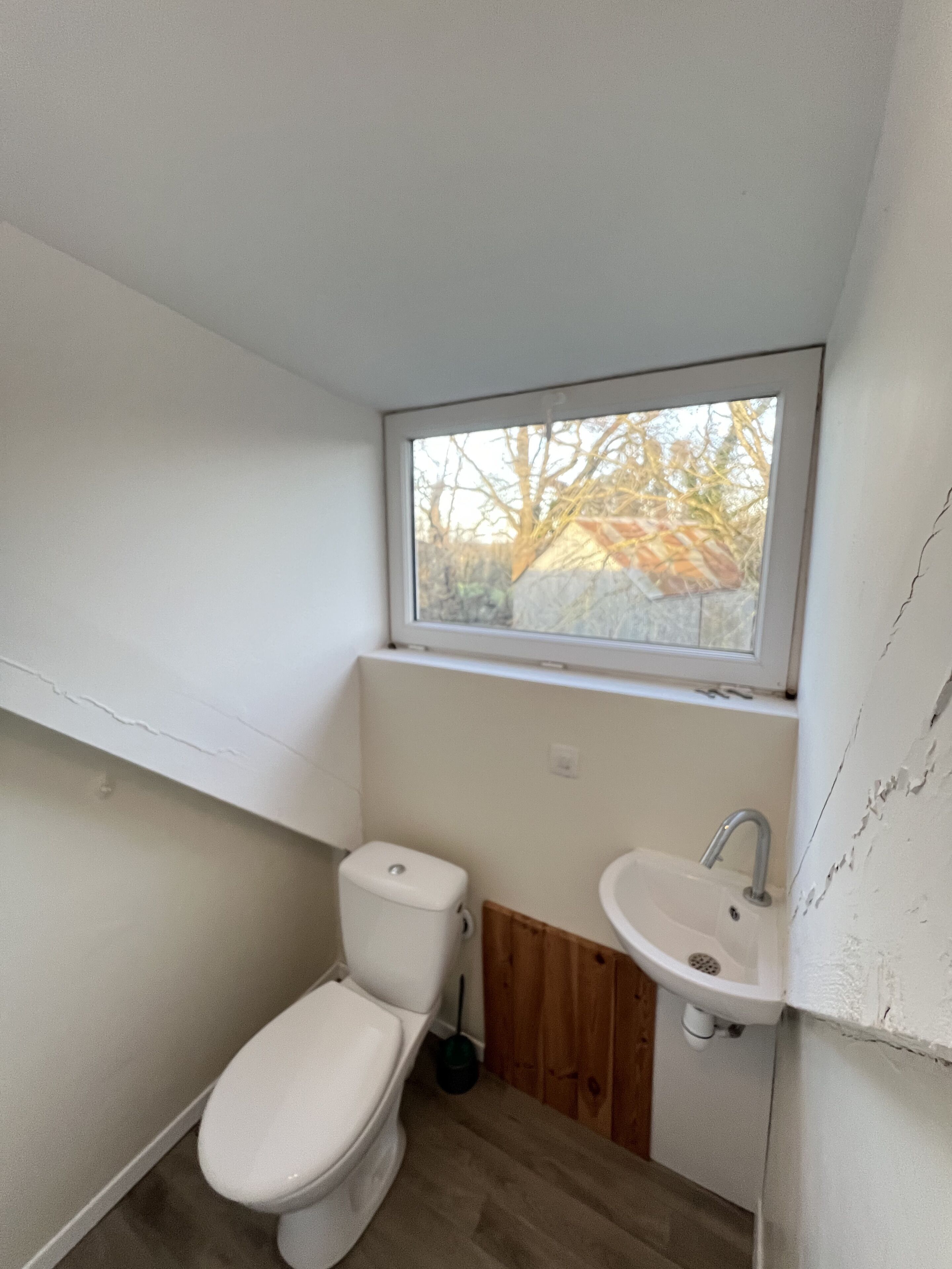 Ein kleines, weißes Badezimmer mit Toilette, Waschbecken und Fenster.