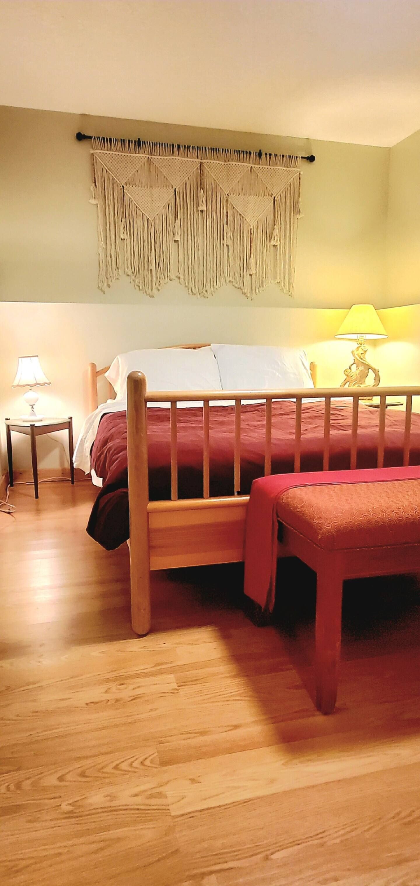 A bedroom with a wooden bed, a nightstand with a lamp, and a wall hanging.