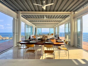 Une salle Ă manger spacieuse avec vue sur lâocĂ©an, un ventilateur de plafond et une table dressĂ©e pour le repas.