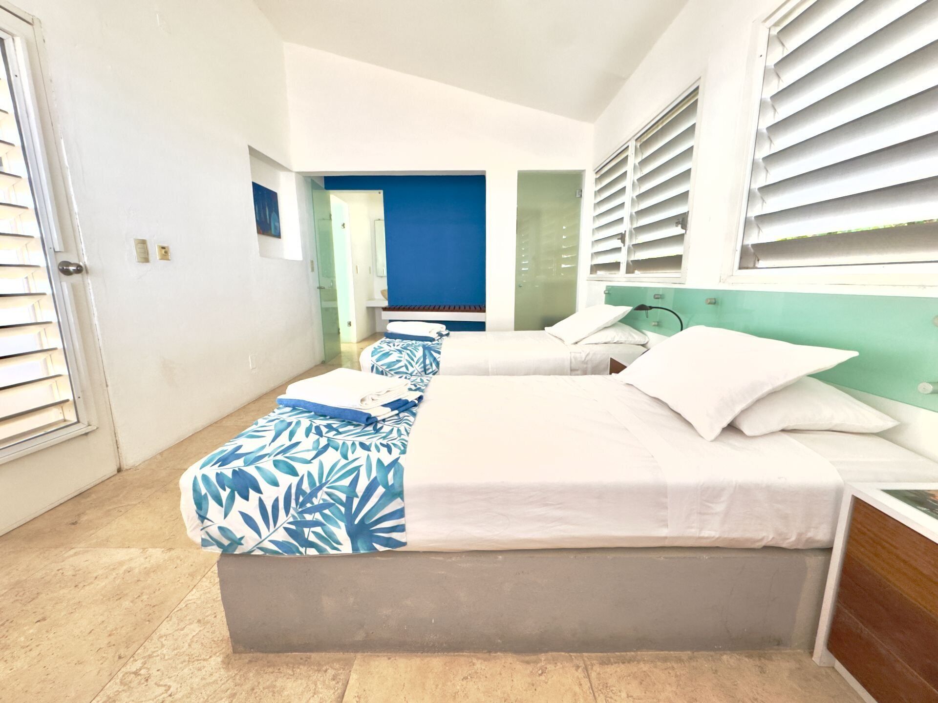 A hotel room with two beds, a bathroom, and a view of the street.