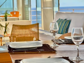 Una mesa de comedor con platos, vasos y una silla en una habitación con vista al océano.