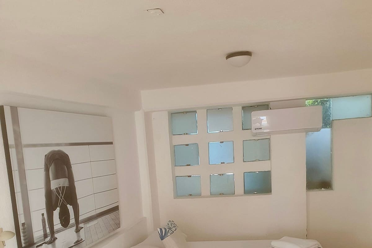 Un dormitorio moderno con una cama grande, un aire acondicionado de pared y una ventana de múltiples paneles.