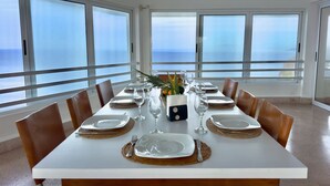 Mesa de comedor preparada para seis personas, con platos blancos, vasos transparentes y manteles individuales marrones.