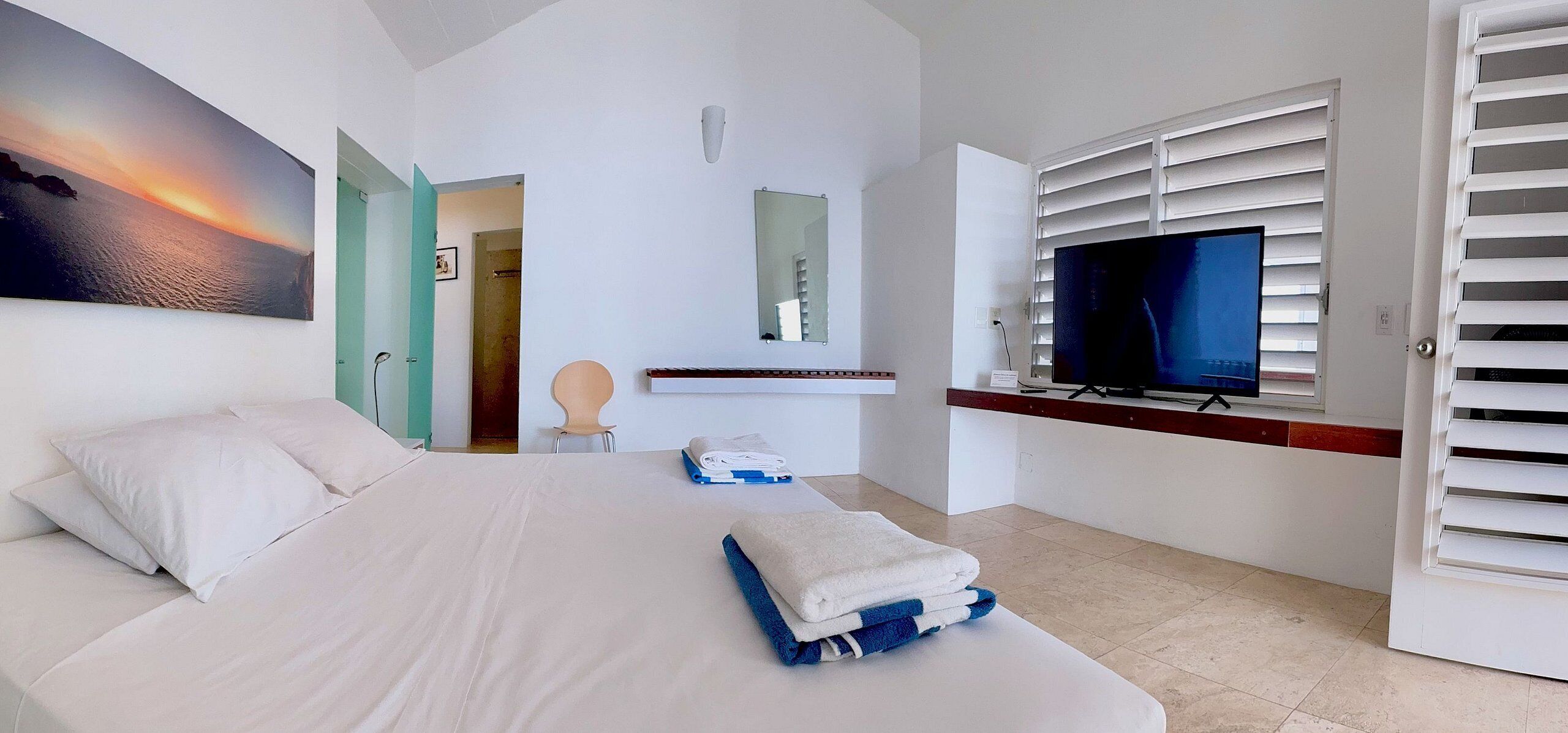 Une chambre d’hôtel avec un lit, une télévision, un tableau et une salle de bain visible à travers une porte ouverte.
