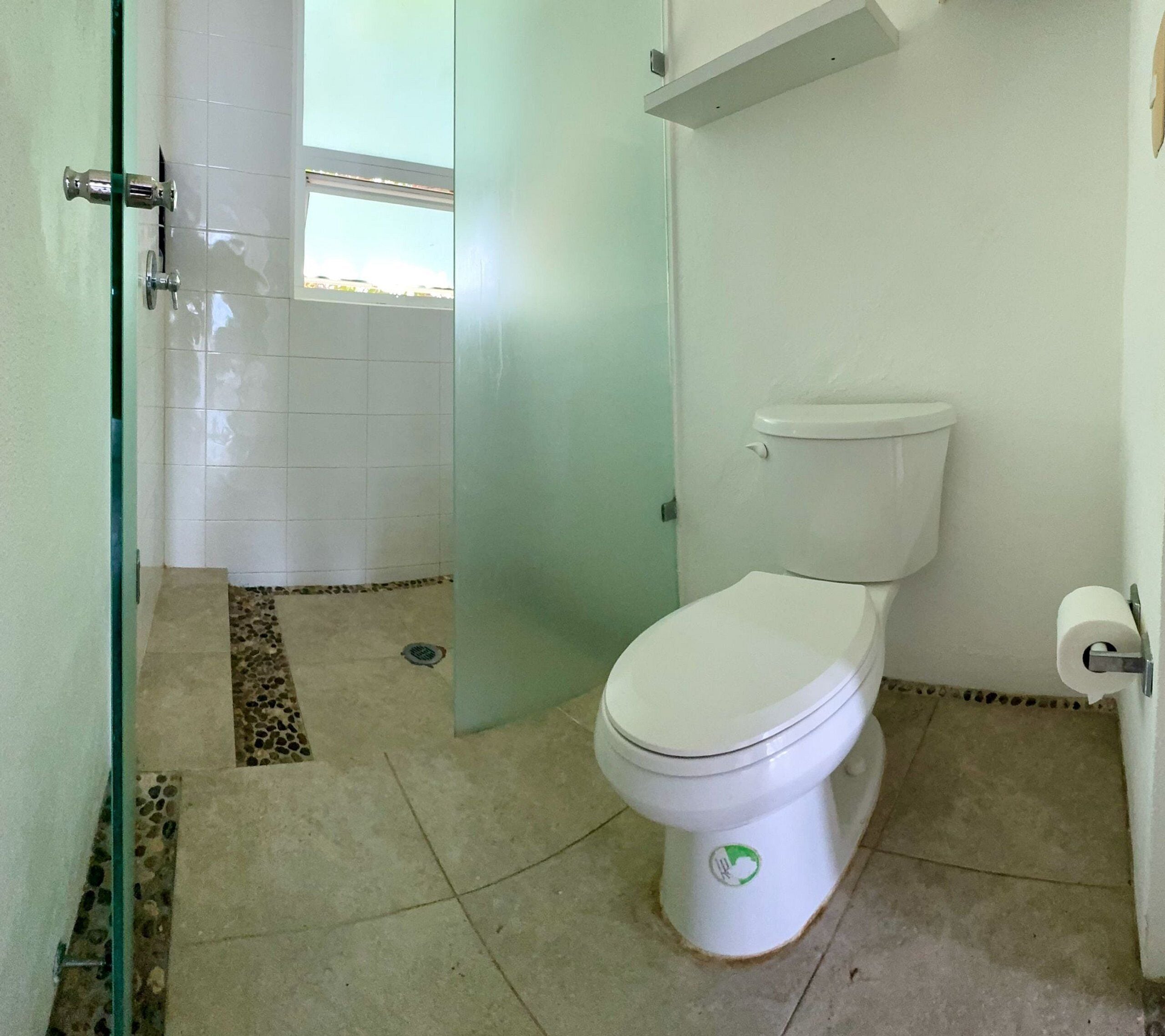 Un baño con inodoro, mampara de vidrio y suelo de baldosas.