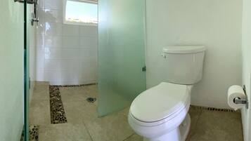 Un baño con inodoro, mampara de vidrio y suelo de baldosas.