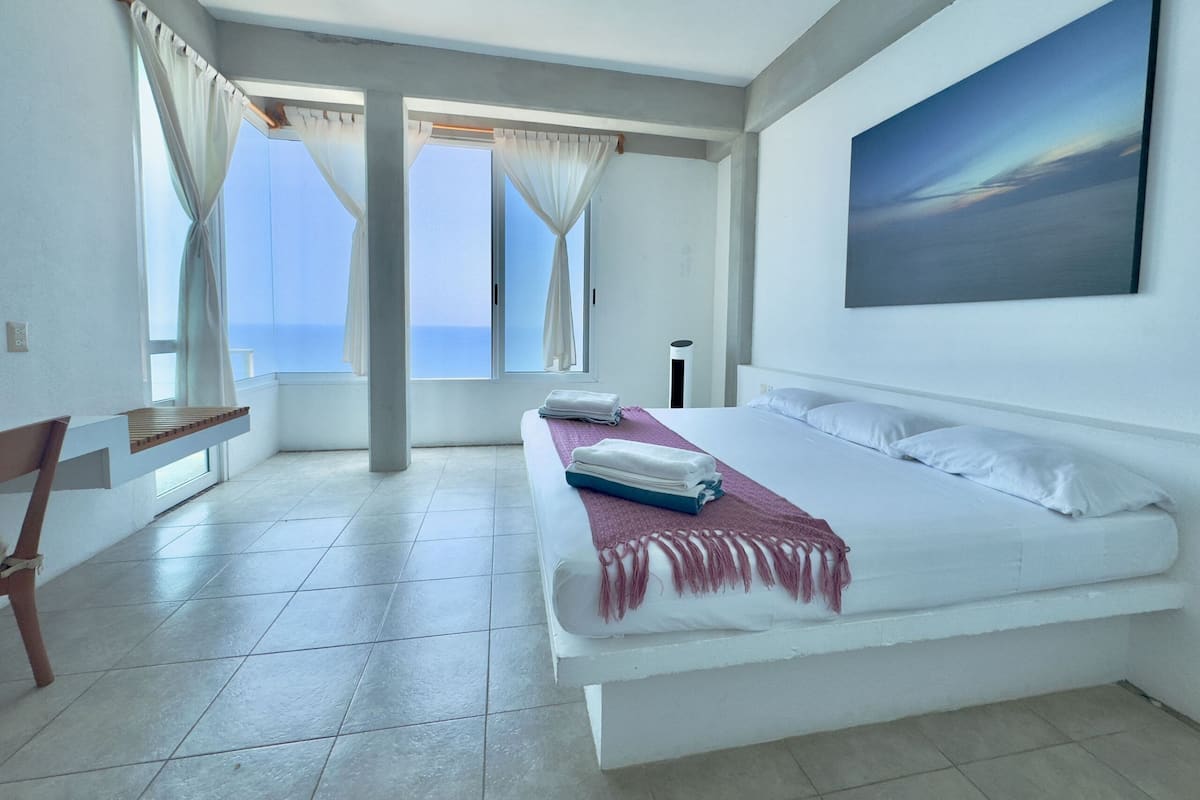 Un dormitorio con cama, escritorio, lámpara de pie y un cuadro en la pared.