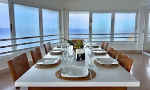 Mesa de comedor preparada para seis personas, con platos blancos, vasos transparentes y manteles individuales marrones.