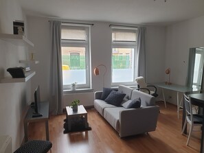 Una sala de estar moderna con un sofá gris, una mesita, un escritorio con silla y un ventanal con cortinas.