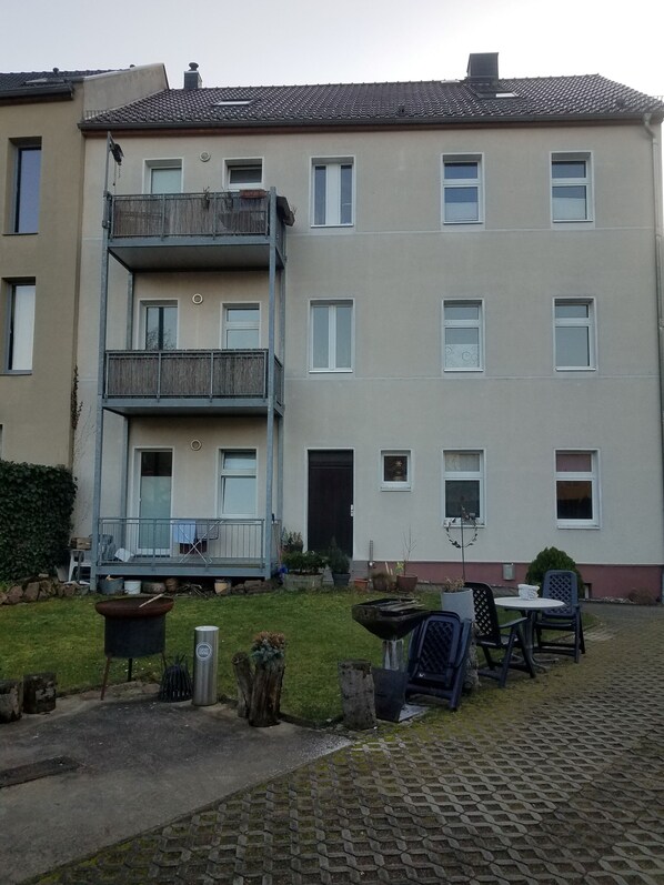 Un edificio residencial de varios pisos con un balcón, un pequeño jardín y asientos al aire libre.