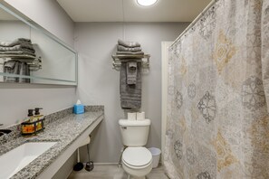 Ein Badezimmer mit einer weißen Toilette, einem Waschbecken mit Marmorplatte, einem Handtuchhalter mit gefalteten Handtüchern und einem Duschvorhang mit Blumenmuster.