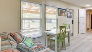 A room with a sofa, a table, and a chair. There are windows with blinds, a door, and a wall with a zebra painting. - Horse Farm Cottage Near WEC + Rainbow Springs (Morriston)