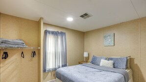 A bedroom with a bed, a nightstand, a lamp, a window with curtains, and a wall-mounted shelf with folded towels. - Cottage on 80-Acre Farm near WEC & Devil's Den (Morriston)