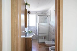 A modern bathroom with a wooden vanity, a glass shower enclosure, and a white sink.