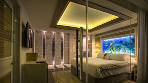 A modern bedroom with a large bed, a glass partition, a television, and a wall aquarium. - Private Paradise Villa (Cozumel)