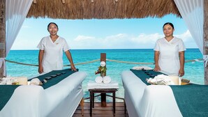 A spa room with two massage tables, a small table with candles and flowers, and a view of the ocean. - Private Paradise Villa (Cozumel)