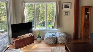 A living room with a television on a wooden cabinet, a potted plant, and two stacked ottomans.