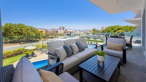 A balcony with a sofa, chairs, a table, and a view of a swimming pool and cityscape. - Increible y Moderno Departamento con Mucho Espacio, Ideal Para Quien sea (Bucerías)