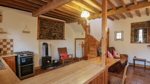 A rustic kitchen with a wood stove, a stone wall, and a wooden staircase.