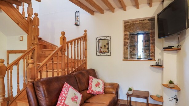 A living room with a brown leather sofa, wooden staircase, stone wall, and a mounted TV.