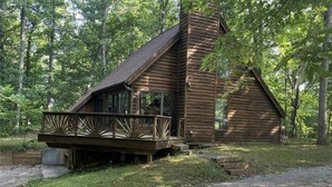 A wooden cabin with a deck and a chimney, surrounded by trees.