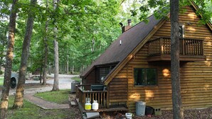 A wooden cabin with a balcony, surrounded by trees.