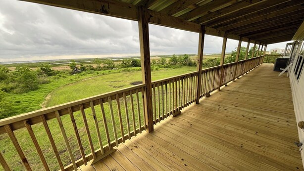 A wooden deck with a railing overlooking a grassy landscape.