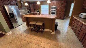 A kitchen with a central island, stainless steel appliances, wooden cabinets, and a tiled floor.