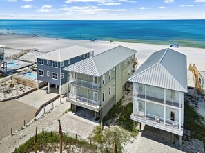 En fastighet vid stranden med flera byggnader, inklusive ett stort hus med en balkong och en mindre byggnad med en pool.