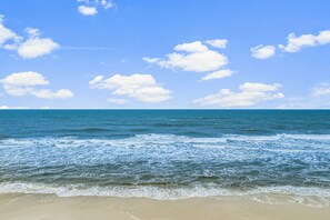 Een strand met helderblauw water en witte wolken.