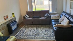 A living room with a brown sofa, a black leather sofa, a patterned rug, a fireplace, and a window with curtains. - Detached 4-bed House in Leeds (Leeds)