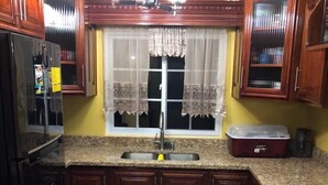 A kitchen with wooden cabinets, a sink, a stove, and a window with curtains. - Lapiz Lazuli at Serenity Palms (Runaway Bay)