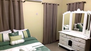 A neatly made bed with green bedding and pillows, a white dresser with a mirror, and brown curtains. - Lapiz Lazuli at Serenity Palms (Runaway Bay)