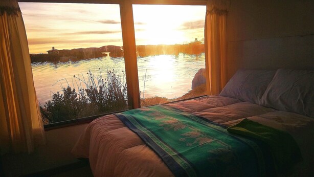 A bedroom with a large window overlooking a body of water during sunset. - Room-lucsay Habitacion Vista Al Amanecer (Puno)