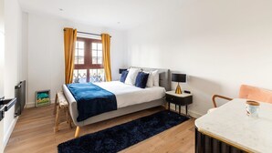 A modern bedroom with a bed, bedside table, lamp, chair, and a view of the city through a window. - City View Spacious 2 Bedroom Penthouse (London)