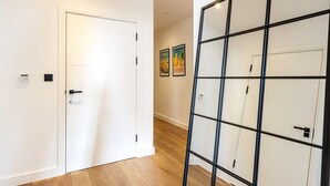 A hallway with a white door, a black-framed glass partition, and a wooden floor. - City View Spacious 2 Bedroom Penthouse (London)