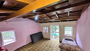 A room with a patterned floor, a bed with floral bedding, a window with a view, and a ceiling with exposed beams. - The Gazzaar Riverside camp (Nainital)