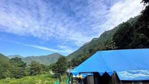 A tented area with a table and chairs, surrounded by greenery and hills. - The Gazzaar Riverside camp (Nainital)