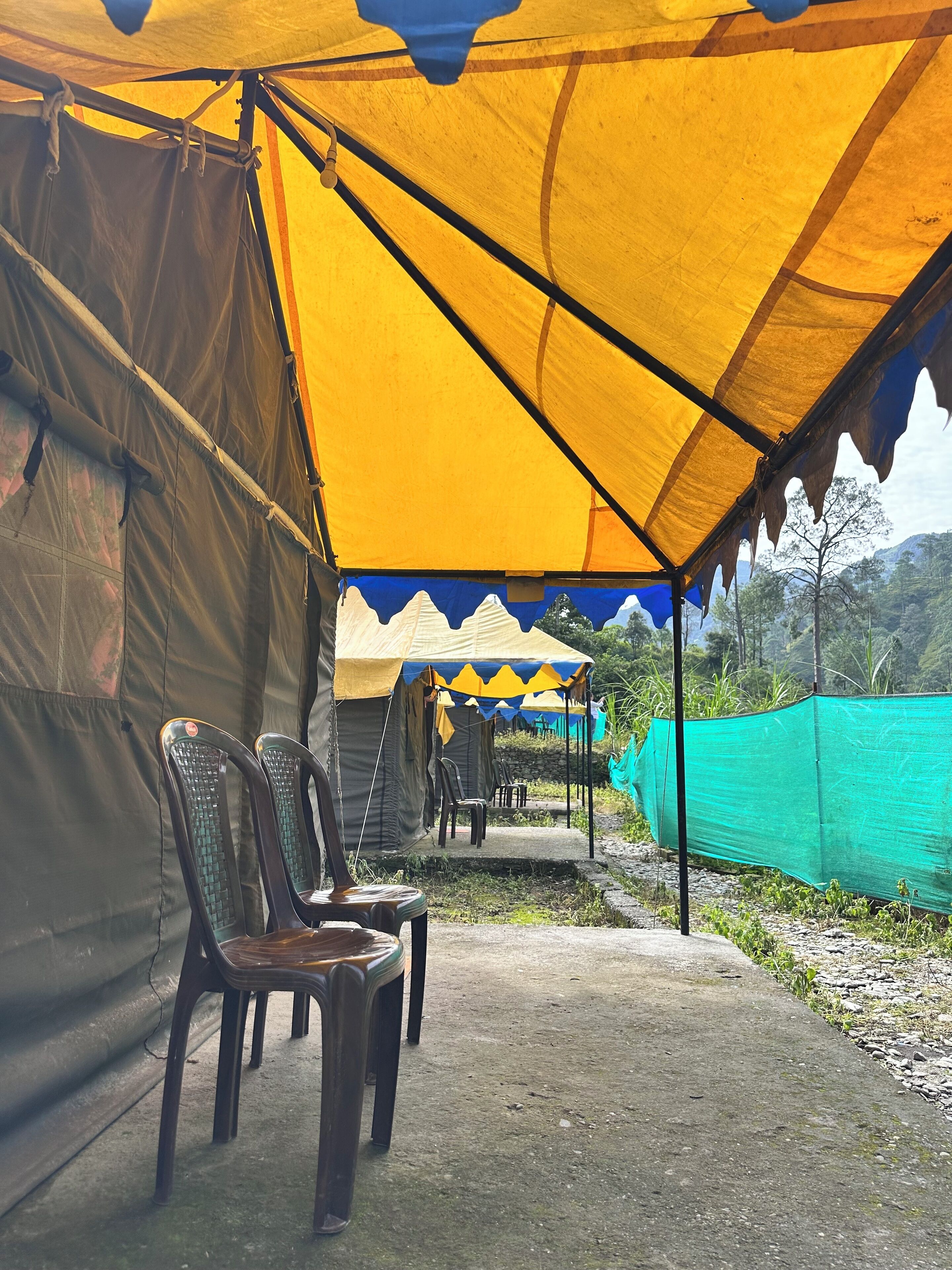 A series of tents with yellow and blue tarps, plastic chairs, and a green netting fence.