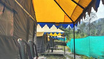 A series of tents with yellow and blue tarps, plastic chairs, and a green netting fence.