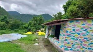 A rustic building with a colorful exterior, surrounded by lush greenery and mountains in the background. - The Gazzaar Riverside camp (Nainital)