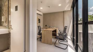 A modern office space with a wooden desk, two black office chairs, a whiteboard, and a window with a view of buildings and trees.
