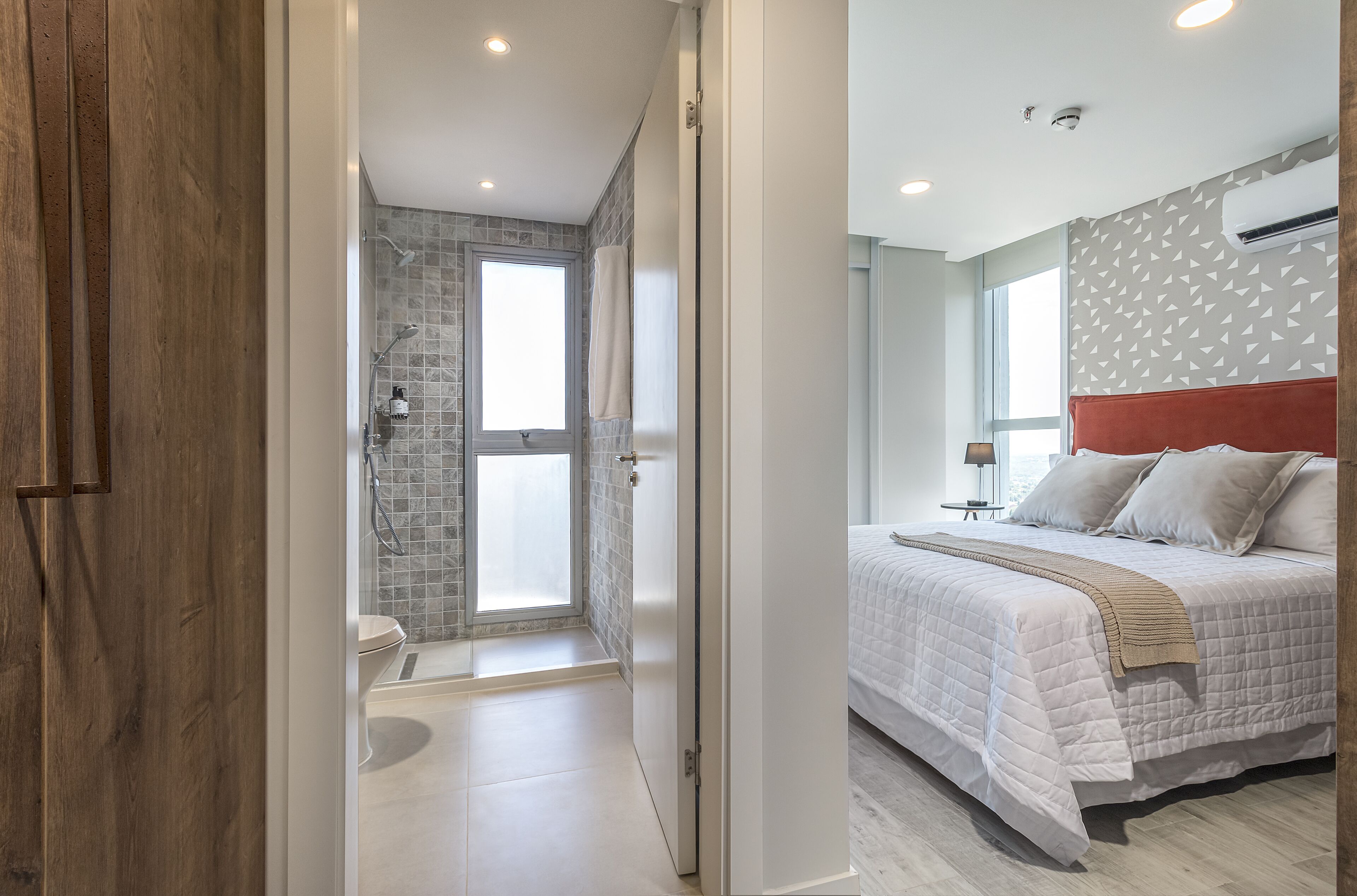 Quarto moderno com uma cama grande, uma porta de madeira e banheiro com chuveiro e janela.